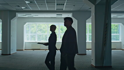 Fototapeta premium Businesspeople silhouettes crossing hall. Woman man discussing work together