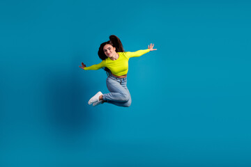 Young woman in stylish yellow top jumping joyfully against blue background symbolizing happiness
