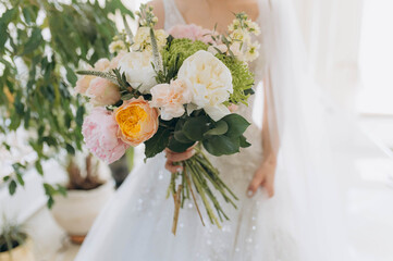 A stunning bouquet features peonies, roses, and greenery. The bride displays the bouquet in a beautifully lit setting.