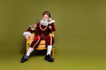 A Senior Man in Renaissance Noble Costume Sitting on a Golden Chair Against Khaki Background