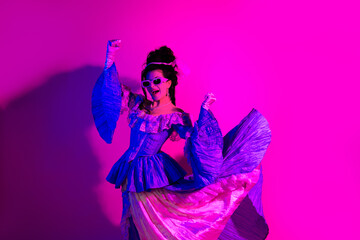 Elegant young woman in vintage baroque gown posing with modern neon lighting against a vibrant background of ultraviolet pink hues