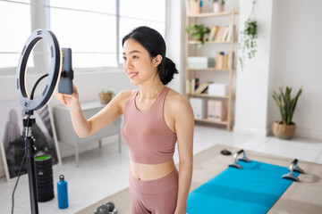 Young sportive fitness instructor streaming training class at home, preparing smart phone app to record social media content.