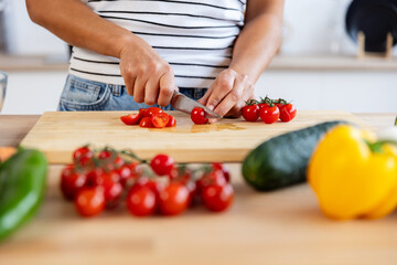 Woman slicing fresh cherry tomatoes on a wooden board, surrounded by various vegetables, embodying healthy eating and home cooking. Healthy lifestyle and food concept
