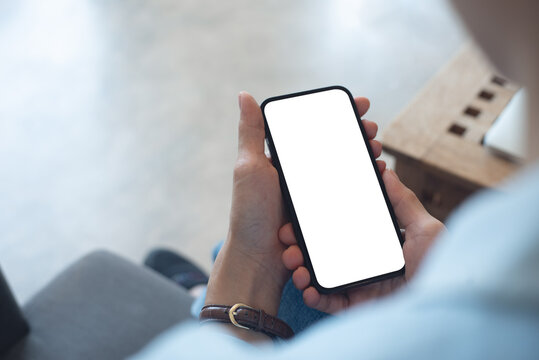 Mockup, woman's hands holding mobile phone with blank screen in coffee shop. Woman using smartphone, looking at the screen, over shoulder view