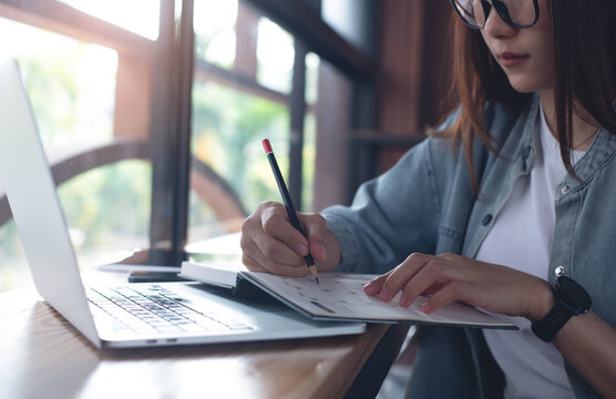 Young asian business woman planning on calendar planner, online working at coffee shop. Female student writing, scheduling plan on paper note book, e-learning, online studying