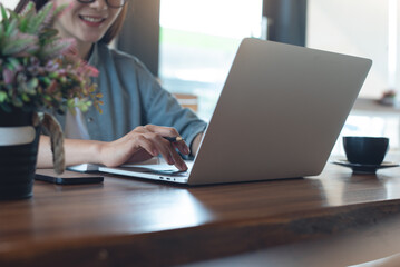 Happy woman sitting in coffee shop, online working on laptop computer, planning work project. Young...
