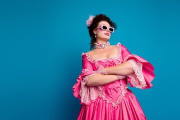Confident woman in pink baroque dress poses against a vibrant blue background, exuding vintage...