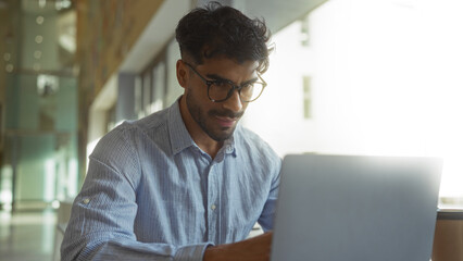 Young man working on laptop in modern clinic with focus on professional and determined expression...