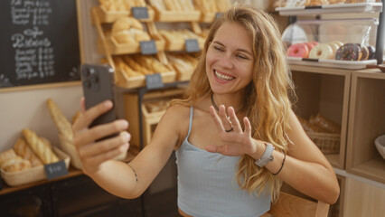 Woman talking on a video call in a bakery shop with various breads in the background, showing a cheerful interaction indoors