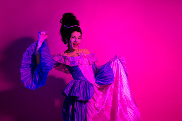 Elegant young woman in vibrant costume posing under neon purple and pink lighting in a baroque inspired artistic setting