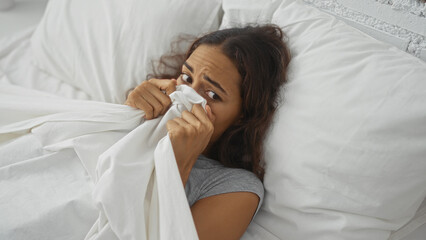 Young woman lying in bed in a bedroom with a scared expression holding a white blanket over her face