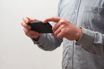 Close-up of a man wearing a gray shirt, holding a smartphone with both hands as if taking a photo or recording a video.