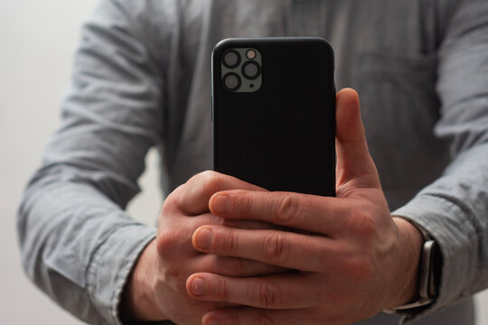 Close-up of a man wearing a gray shirt, holding a smartphone with both hands as if taking a photo or recording a video.