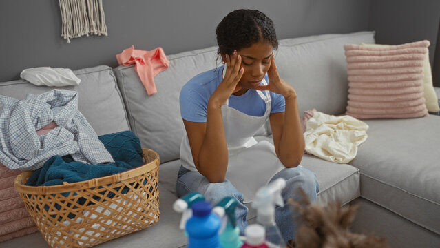 Woman stressed in living room surrounded by laundry and cleaning supplies, highlighting domestic chores and mental load at home