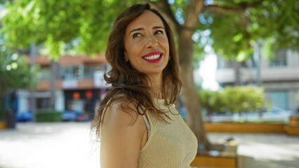 Fototapeta premium Woman smiling in a sunny outdoor urban setting with trees and buildings in the background capturing the essence of a beautiful day
