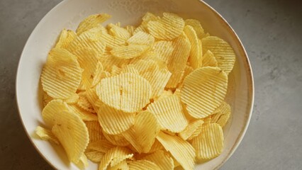 Crispy potato chips served in a bowl placed on a concrete surface highlighting a delicious savory snack ready for casual dining or party gatherings
