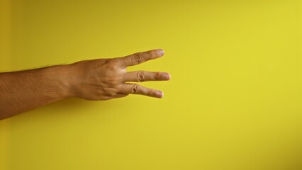 Man's hand showing three fingers against a vibrant yellow background, emphasizing a gesture in a minimalist setting with strong color contrast and simplicity