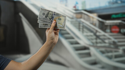 Man holding american money in a shopping center shows hundred dollar banknotes indoors, capturing the essence of spending and wealth in a modern mall setting.