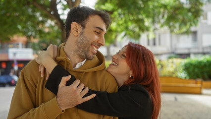 Fototapeta premium Man and woman smiling together in an urban park, showcasing a loving couple in a joyful relationship outdoors, highlighting warmth and connection amidst a vibrant city backdrop.