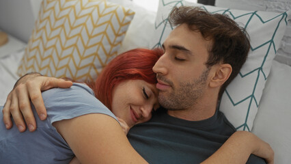 Couple embracing lovingly in a cozy bedroom, woman with red hair gently resting on man's chest,...