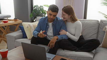 Couple sitting together in a cozy living room, man using laptop while woman leans close, showcasing love and companionship in a modern apartment setting.