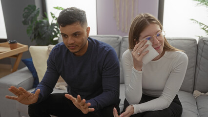 Man and woman sitting on couch in living room, woman wiping tears with tissue, emotional couple sharing intimate moment, cozy home setting, casual clothing, afternoon light
