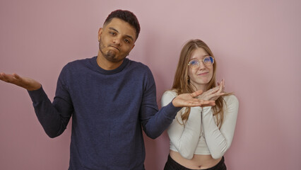Obraz premium Man and woman shrugging together in front of an isolated pink wall background expressing confusion and uncertainty with casual outfits.