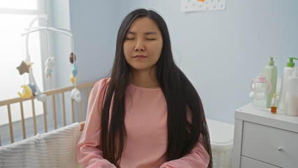 Woman meditating in a cozy baby room with a cradle, surrounded by soft pastel interiors and baby items.