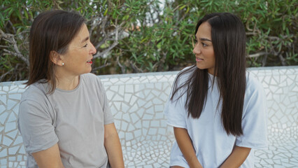 Mother and daughter having a heartfelt conversation in an outdoor park setting surrounded by lush greenery, showcasing family love, bonding, and connection between the two women.
