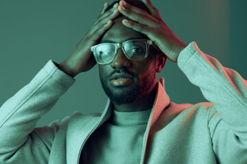 A thoughtful young man wearing glasses and a light sweater, expressing contemplation with a hand on...