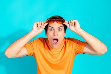 Surprised Young Man Touching Sunglasses on Bright Turquoise Background, Expressing Amazement and...
