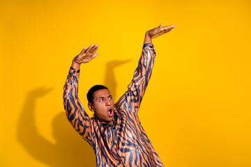 Young man posing playfully against vibrant yellow background wearing a stylish patterned shirt
