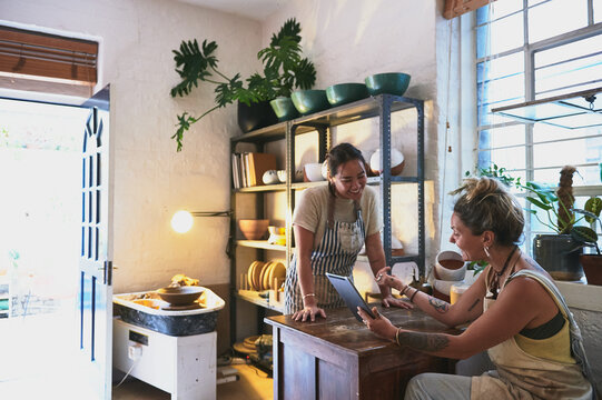 Small business, workshop and people with tablet at pottery shop on social media for customer reviews. Women, partners and team at startup on web for online post, blog engagement or ratings for art