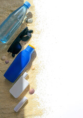 Productos de protección solar, gafas o lentes de sol y botella de agua sobre arena. 