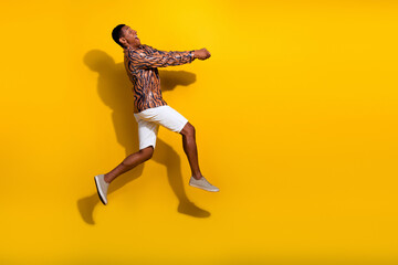 Energetic young male with vibrant style leaping against a yellow background, expressing joy and...