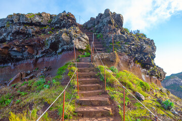 Stone steps leading up a rocky hill, with railing on both sides for support. Steps are surrounded...