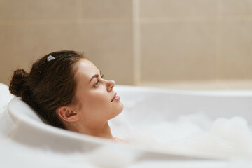 Peaceful young woman relaxing in a bathtub filled with bubbles, enjoying a moment of self-care and tranquility. Wellness and relaxation concept.