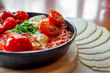 Close up of delicious shakshuka with cherry tomatoes, eggs, and parsley garnished with flatbreads