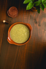 Rustic Green Soup in a Clay Bowl with Wooden Coasters and pepper shaker on a Dark Table