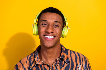 Young stylish man in tiger print shirt and headphones against yellow background