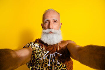 Portrait of aged primeval caveman make selfie wear leopard skin clothes isolated on yellow color background