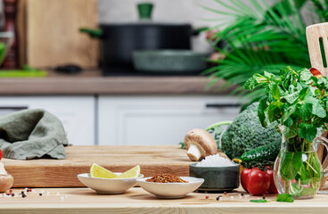 Healthy vegan food, eating, cooking, blogging background. Empty rustic cutting board with mushrooms, tomatoes, lettuce, vegetables on white kitchen with wooden table, kitchenware and utensils.