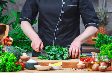 Chef cuts parsley. Cozy kitchen with wooden table, kitchenware, vegetables, herbs and ingredients for cooking. Healthy vegan eating, culinary, recipes, blogging