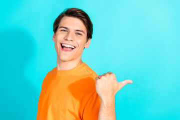 Young man in orange shirt gesturing and smiling against bright turquoise background, expressing...
