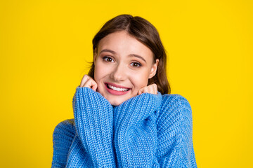 Cheerful young woman in a blue sweater posing against a vibrant yellow backdrop expressing joy and happiness.