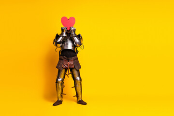 A Young Man in Medieval Knight Costume Holding Red Heart Against Yellow Background