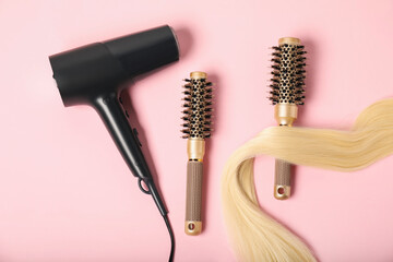 Naklejka premium Stylish round brushes, lock of blonde hair and hairdryer on pink background, flat lay