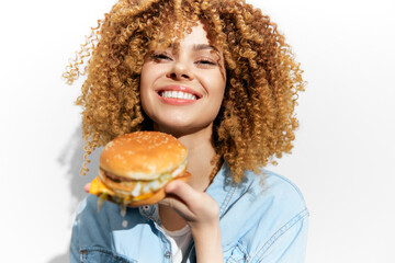 Happy young woman of mixed descent holding a delicious burger with a joyful smile against a bright white background, representing healthy eating and enjoyment