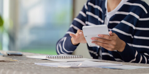 Individual managing financial planning and bills on digital tablet, organizing documents and notes at home.