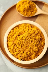Turmeric powder in bowl and spoon on light grey table, top view